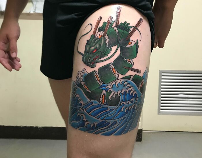 Colorful cool tattoo of a sushi dragon with ocean waves on a person's thigh, showcasing unique and creative body art.