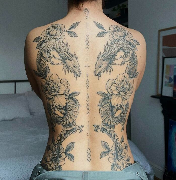 Intricate cool tattoos of dragons and flowers covering full back with symmetrical design and fine line details.