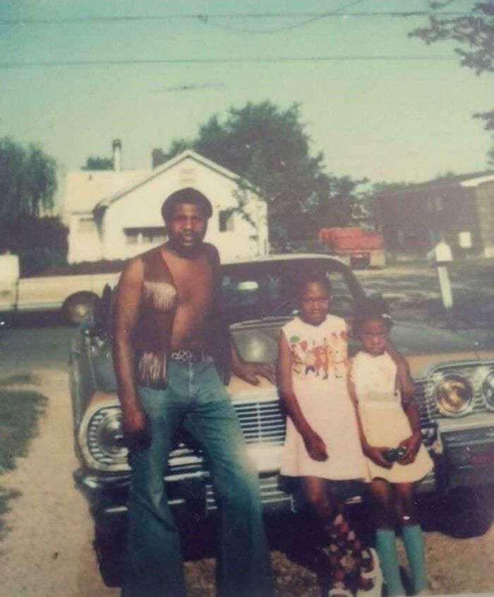 A candid old photo of a man and two girls posing by a car, showing family life generations ago.
