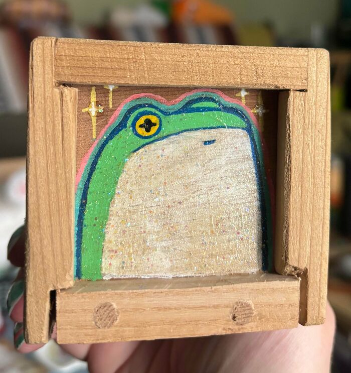 A small wooden box with a hand-painted frog design, sparkling, showcasing a handmade project.