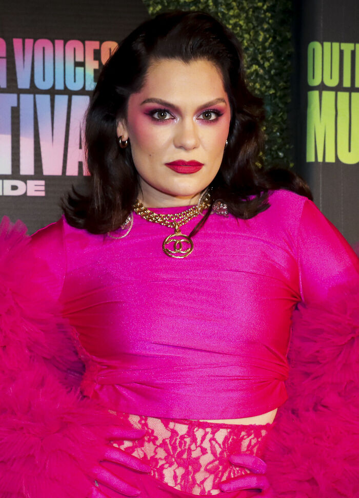 Jessie J in a vibrant pink outfit with bold makeup and gold necklace, posing at a music festival event.