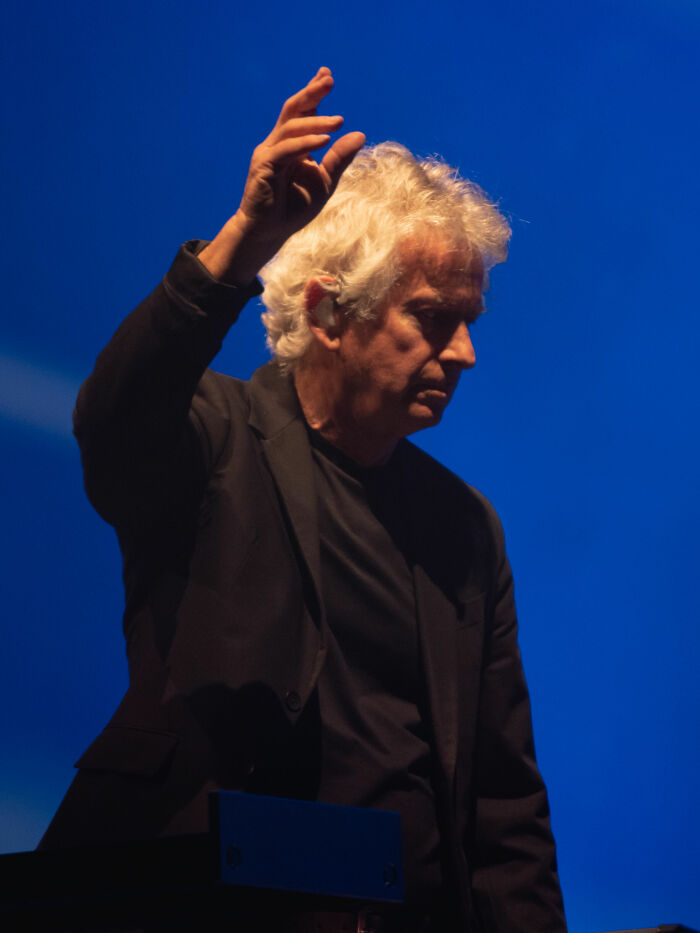 Tony Banks performing on stage with keyboard, highlighting his bio and career highlights in music.