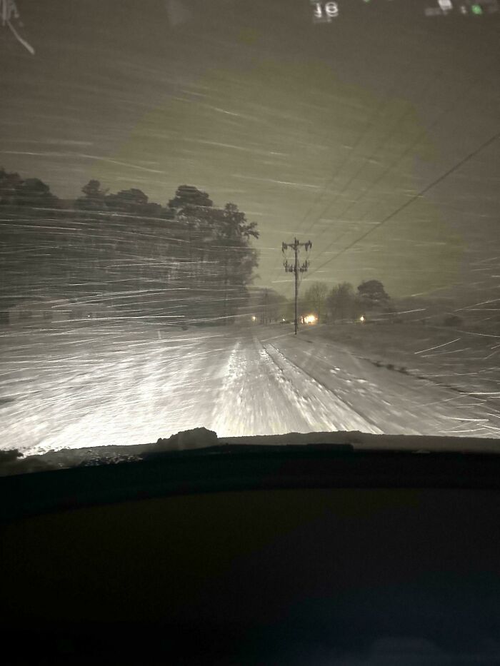 View from inside a car driving through a snowy workplace environment during a harsh winter storm at night.