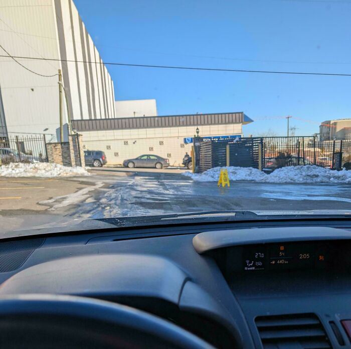 View from car dashboard showing a snowy workplace parking lot under clear blue skies during a cold day.