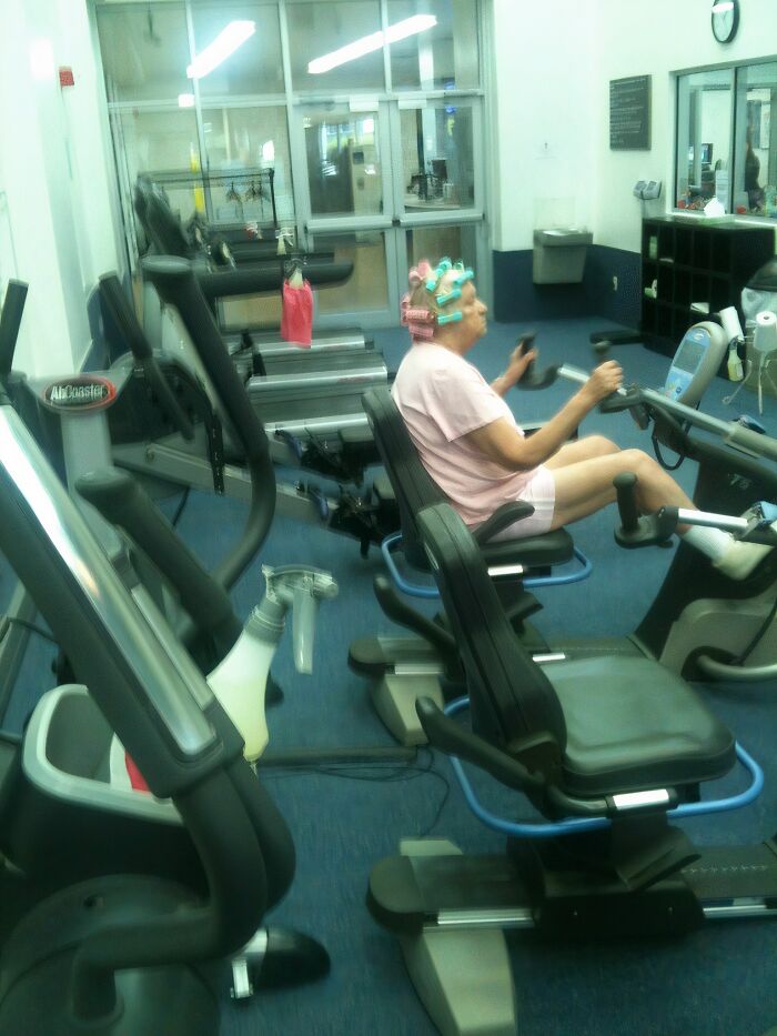 Older woman in hair rollers exercising on a recumbent bike at the gym, an unexpected Darwin Award contender moment.