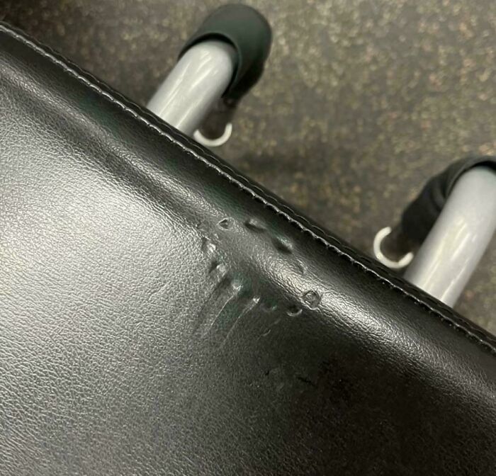 Close-up of damaged gym equipment seat with visible indentations and tears on the black leather surface.