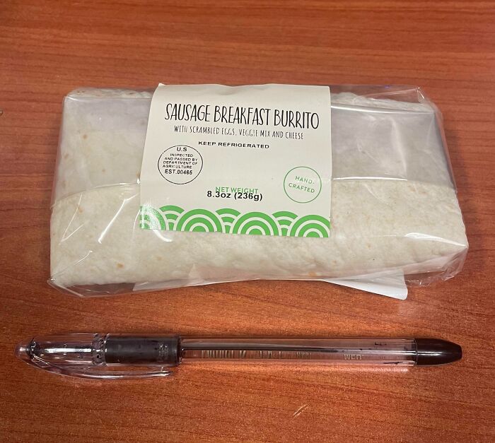 Sausage breakfast burrito on a wooden desk next to a pen, illustrating workplace food choices in office settings.