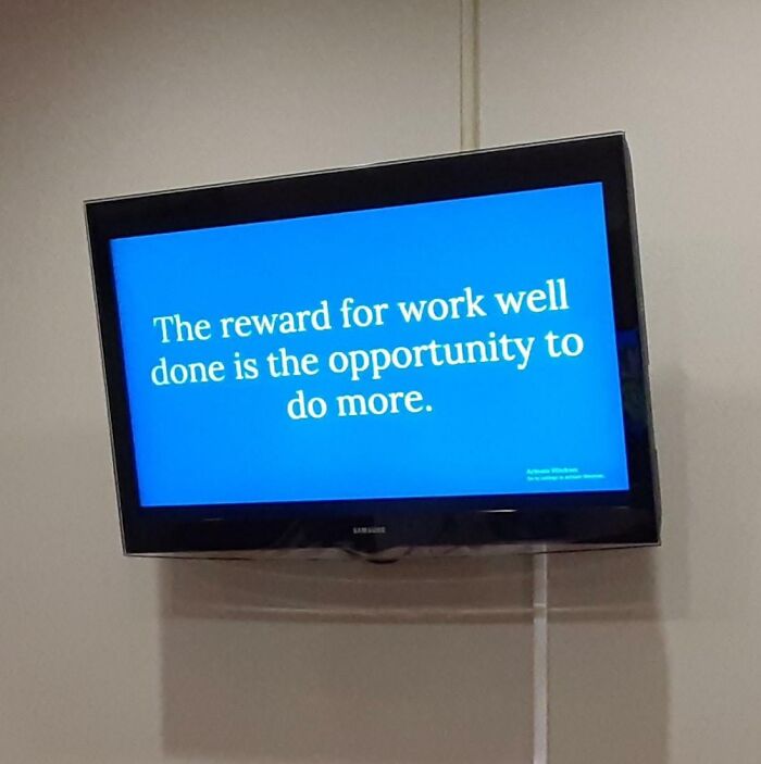 Motivational workplace message on a TV screen highlighting work rewards and the reality of modern work culture.