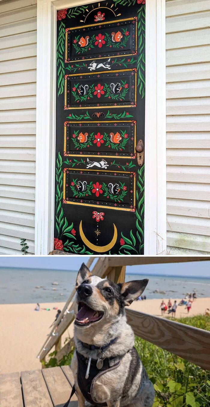 Hand-painted black door with floral and animal designs and a happy dog sitting on wooden steps by the beach.