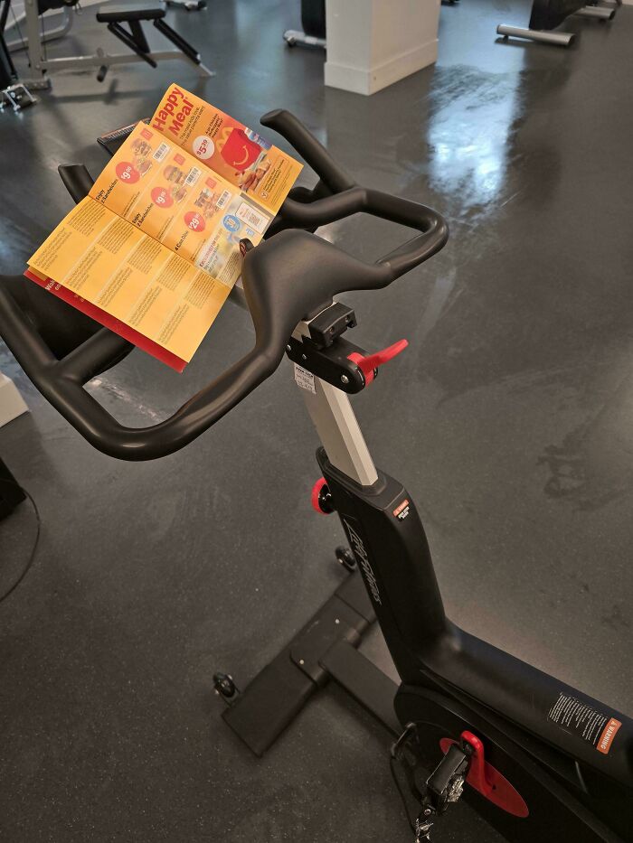 Stationary bike at the gym with a fast food menu placed on handlebars, a gym fail Darwin Award contender moment.