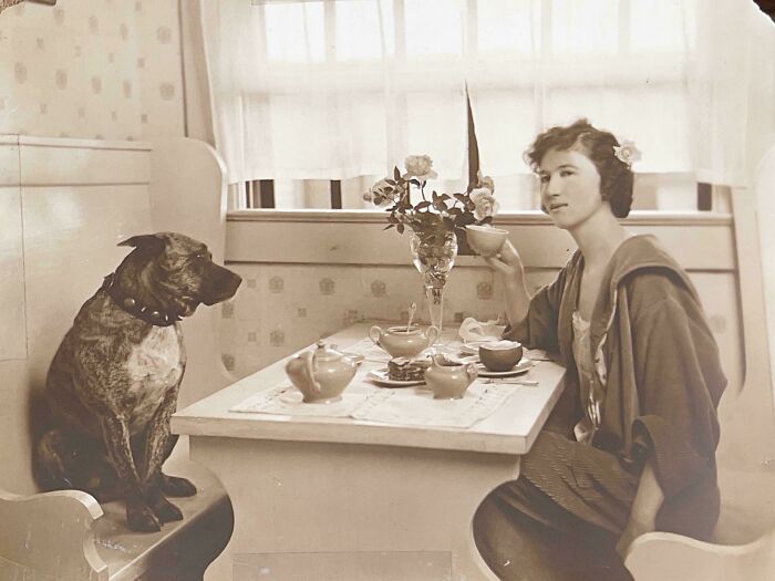 A candid old photo of a woman and her dog at a table, a glimpse into life generations ago.