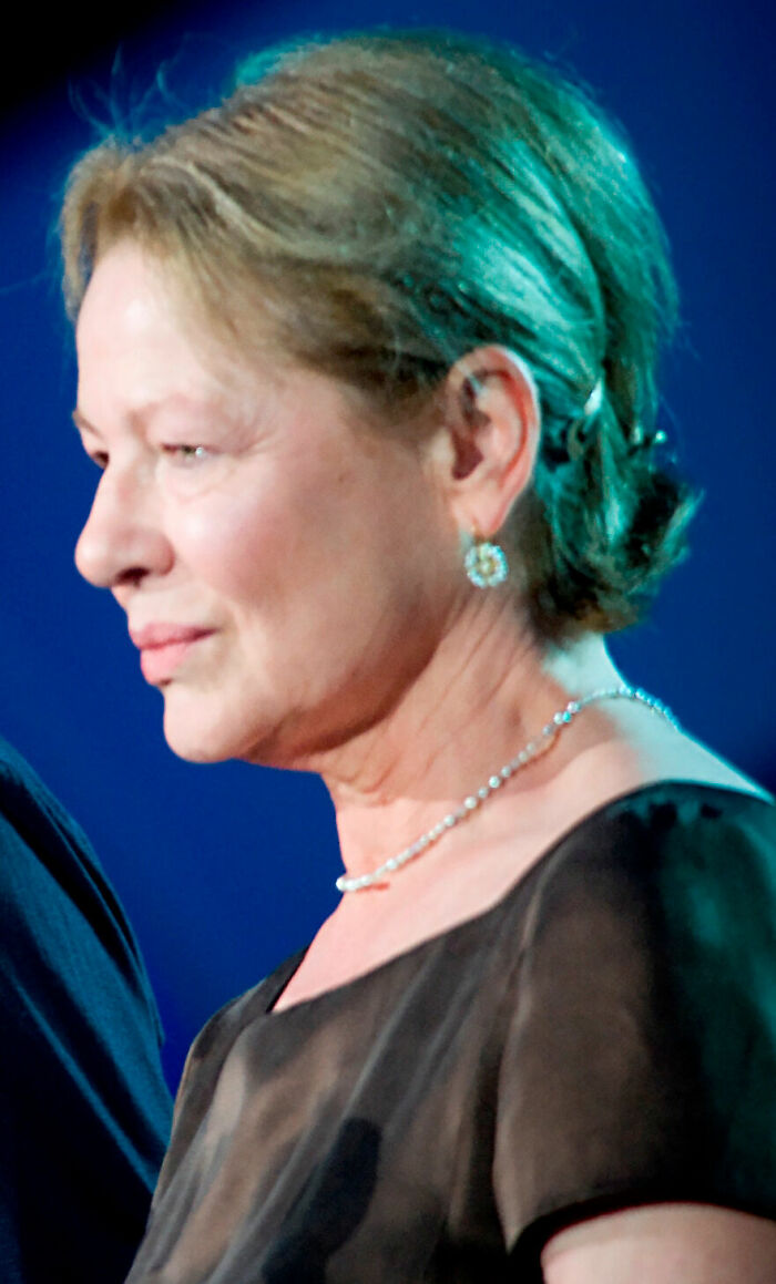 Dianne Wiest in a black dress with pearl necklace and earrings, captured in a close-up side profile at an event.