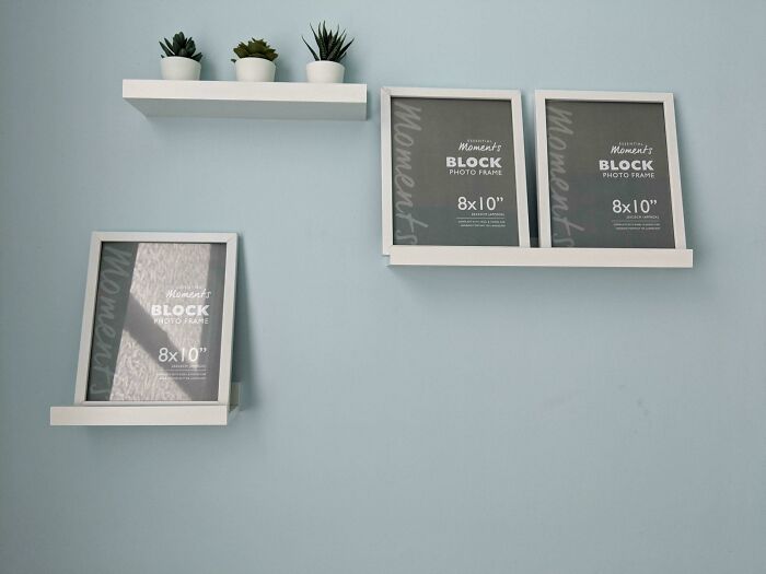 Two wall shelves with picture frames, and a third shelf placed much lower, a funny you had one job fail.