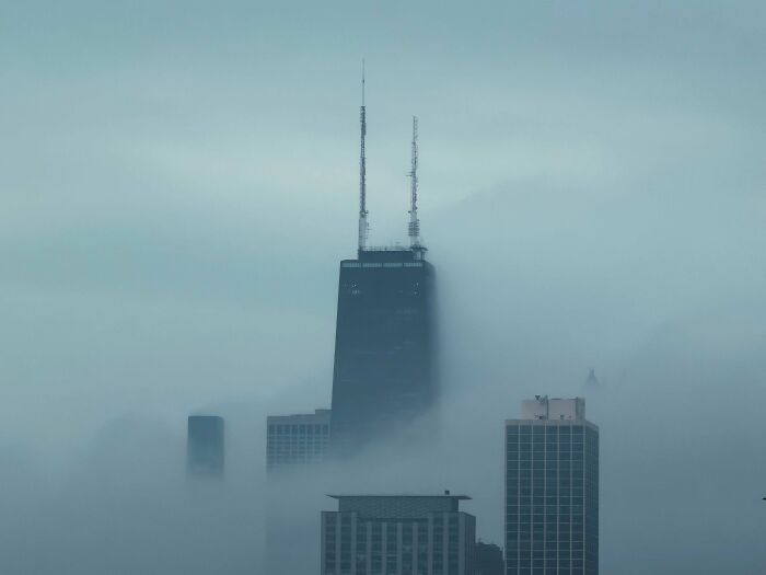 A tall, ominous skyscraper shrouded in thick fog, a perfect hidden lair for an evil mastermind.