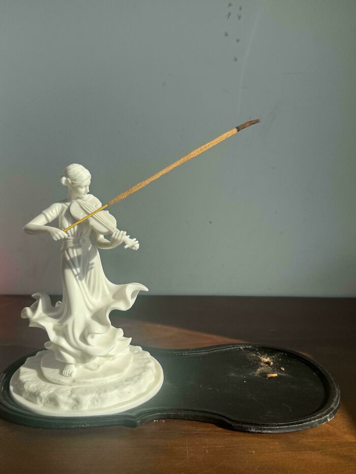 A white ceramic figurine of a woman playing a violin, holding an incense stick as part of a handmade project.