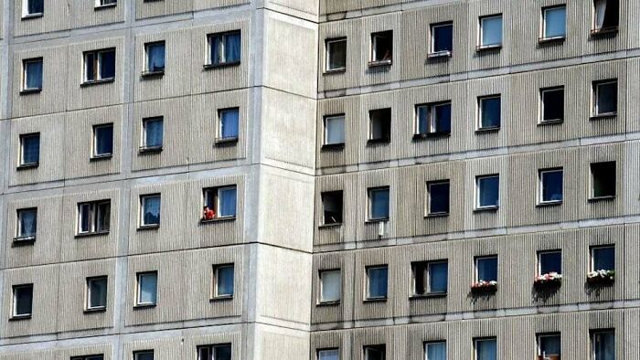 Gray concrete apartment building with many windows, some open and occupied