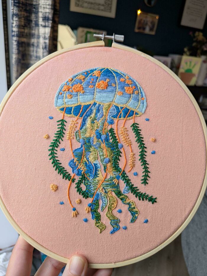 A vibrant embroidery creation of a colorful jellyfish with green seaweed on a pink fabric, inspiring new hobbies.