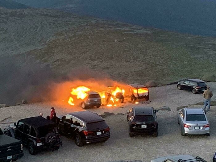 An accidental car fire engulfing vehicles in a parking lot on a mountain, creating dangerous fails.