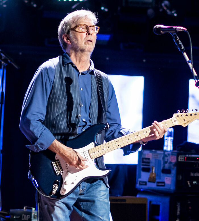 Eric Clapton playing electric guitar on stage during a live performance with microphone and equipment in background