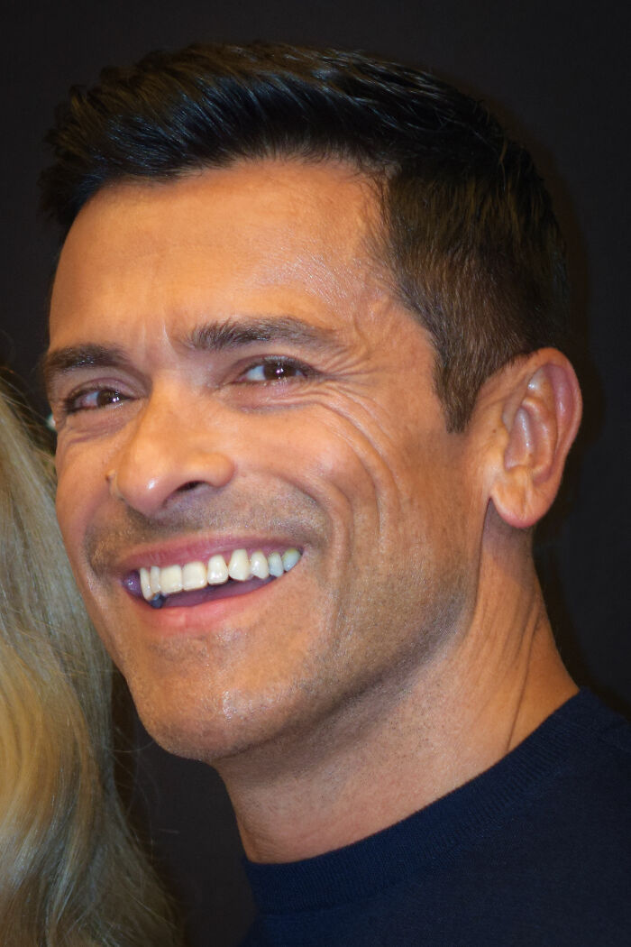 Mark Consuelos smiling with short dark hair and wearing a navy shirt in a close-up portrait for bio and career highlights.