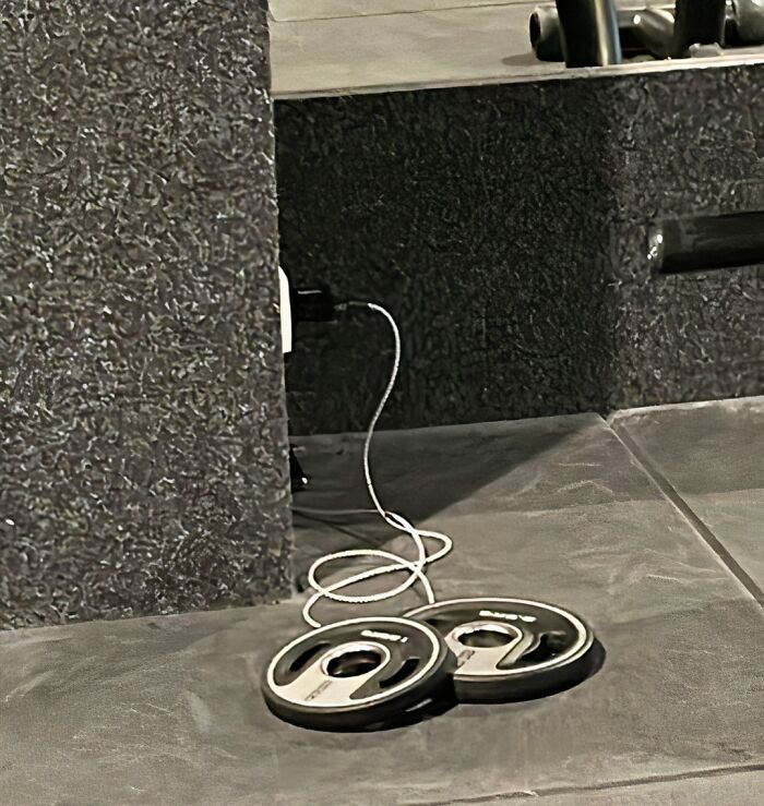 Gym scene with two weight plates connected by a tangled charging cable on the floor, highlighting a gym fail.
