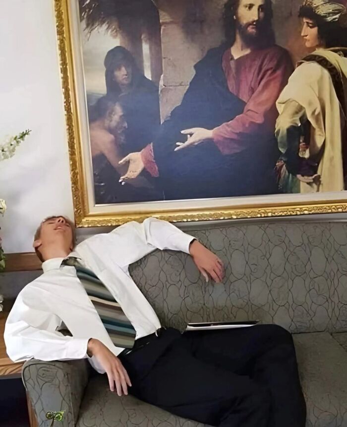 Man in white shirt and striped tie pulling off a creative pose while leaning back on a couch beneath a painting.