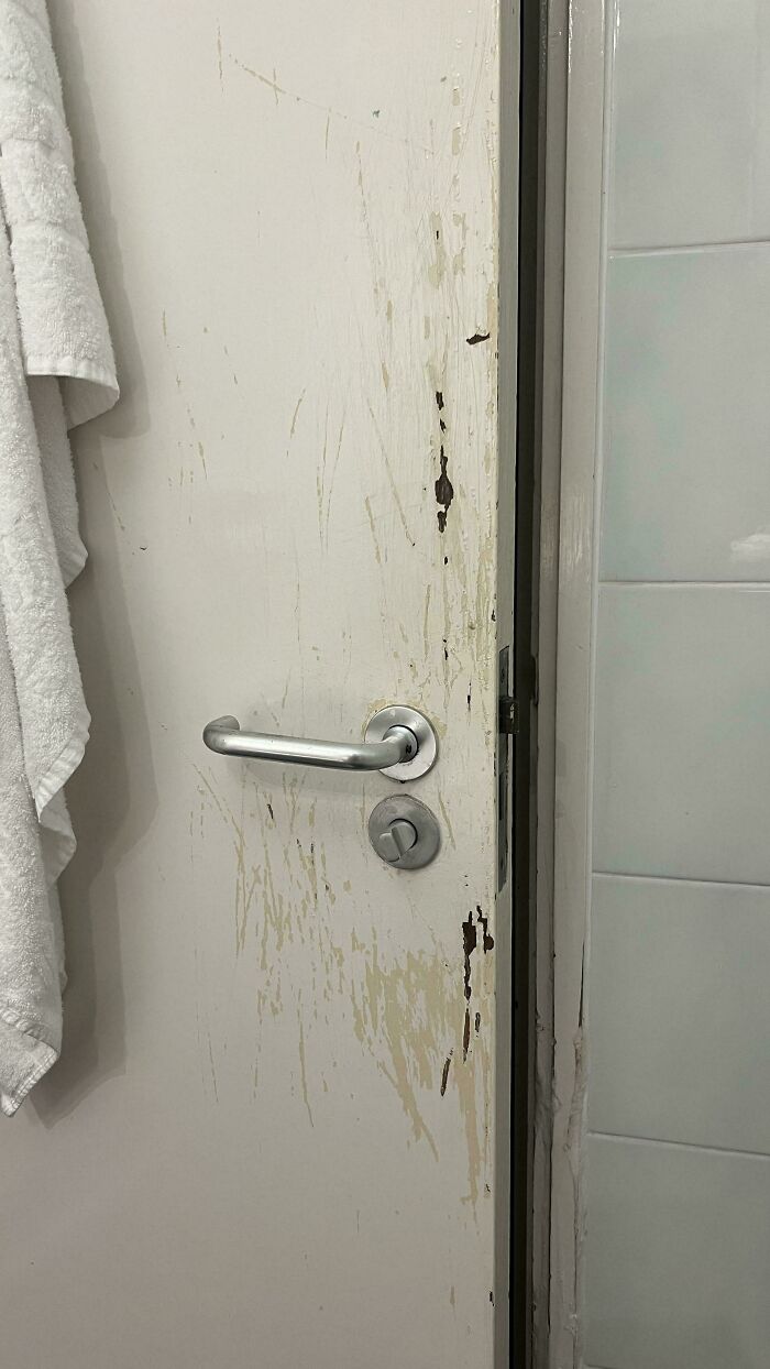 Worn bathroom door with chipped paint and scratches next to white towel and tiled wall, creepy and weird photo.