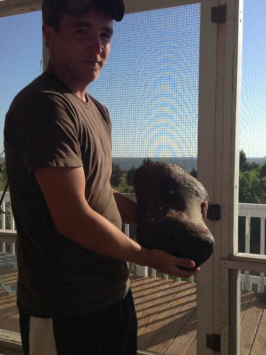 Man holding a large fossil outdoors on a porch with natural scenery in the background, showcasing interesting fossils.
