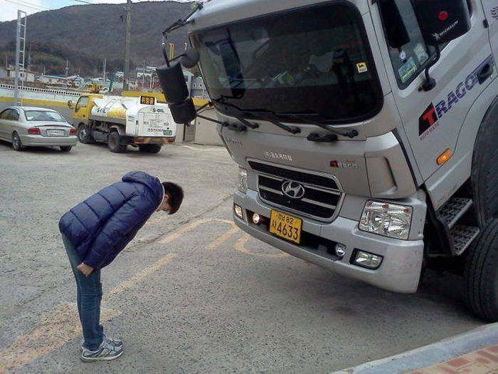 Person creatively posing by bowing toward a tilted truck, showcasing one of the hilarious and creative poses pulled off perfectly.