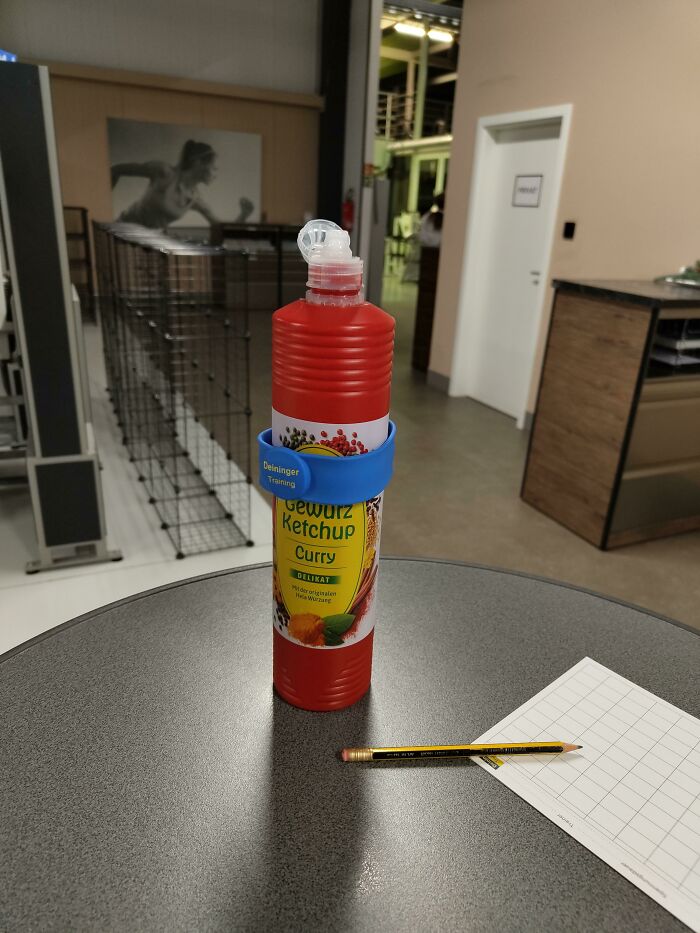 Bottle of curry ketchup with a blue fitness wristband on a gym table next to a pencil and a workout log sheet.