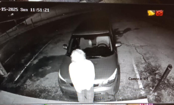 Surveillance image showing a glowing figure standing in front of a car at night, evoking creepy and weird photo vibes.