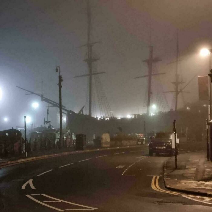 Foggy night scene with a creepy old ship silhouette and dim streetlights creating a weird, eerie atmosphere.