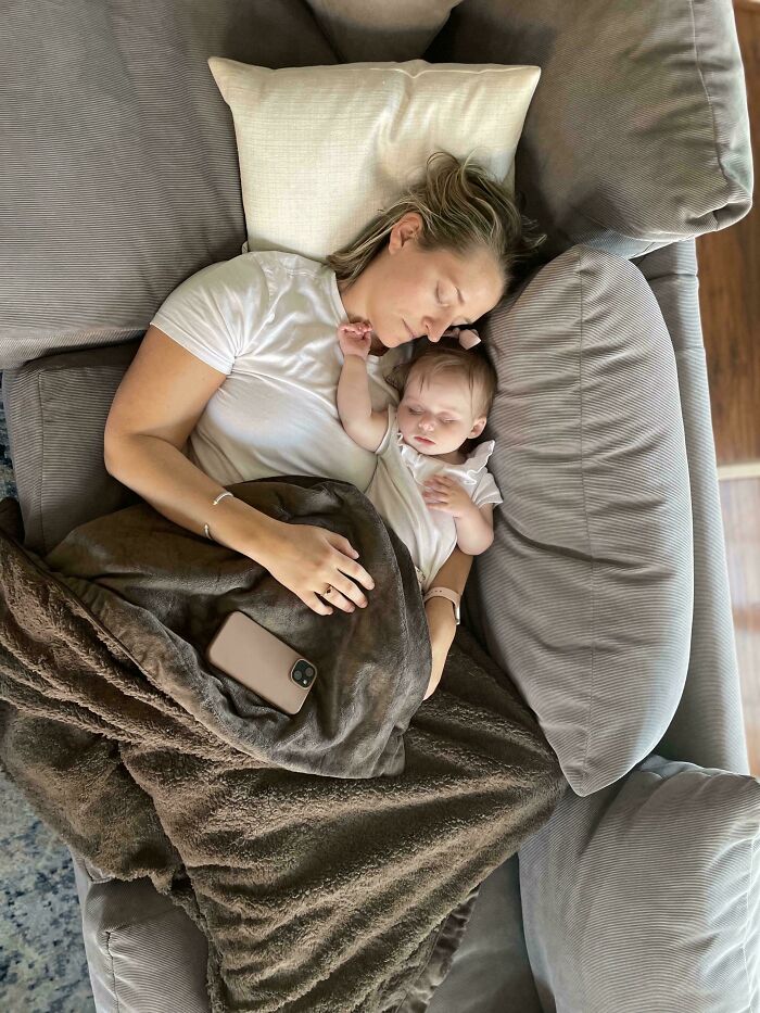 A mother and her baby sleeping peacefully on a grey sofa, reminiscent of an Accidental Renaissance painting.