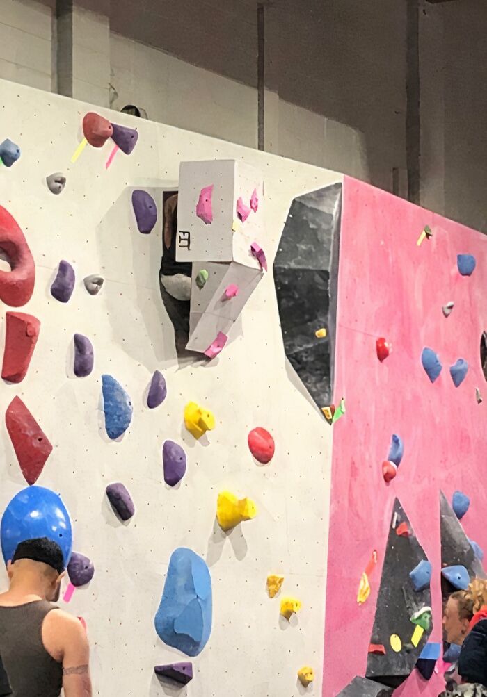 Indoor rock climbing wall with colorful holds and people preparing to climb at a gym Darwin Award contender moment.