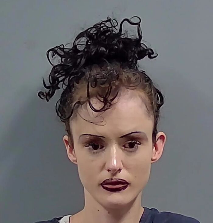 Young woman with crazy eyebrows and curly hair styled atop her head, wearing dark lipstick and a serious expression.