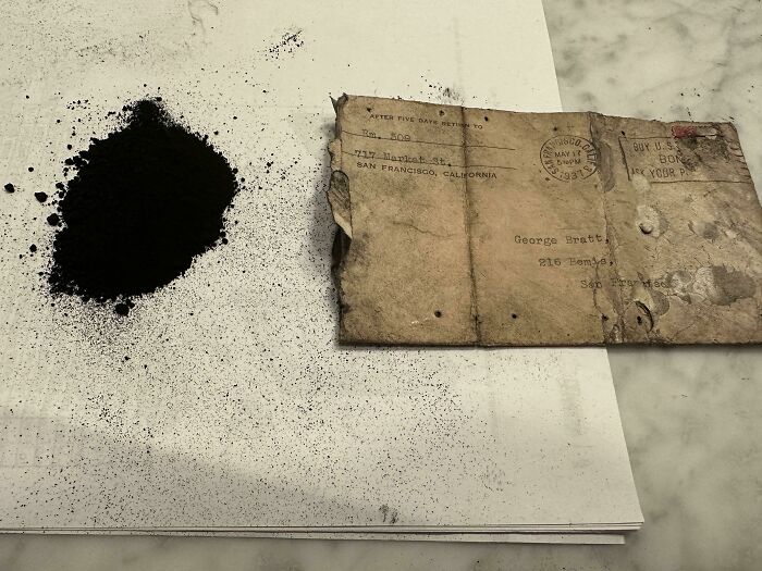 Old stained letter and a pile of black powder on a white surface, evoking unsettling mysteries and eerie unknowns.