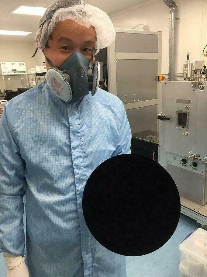 Person in protective suit and respirator holding a perfectly black object that creates a creepy and weird visual effect.