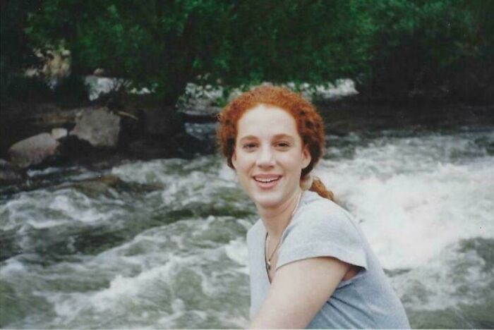 Young woman with red hair smiling near a flowing river, evoking unsettling mysteries that continue to fascinate and disturb readers.