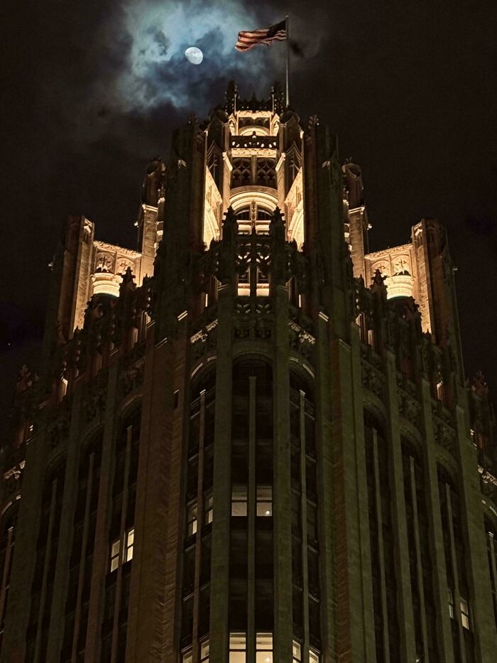 A majestic, illuminated building at night with a full moon and flag, ideal for an evil mastermind's plans.