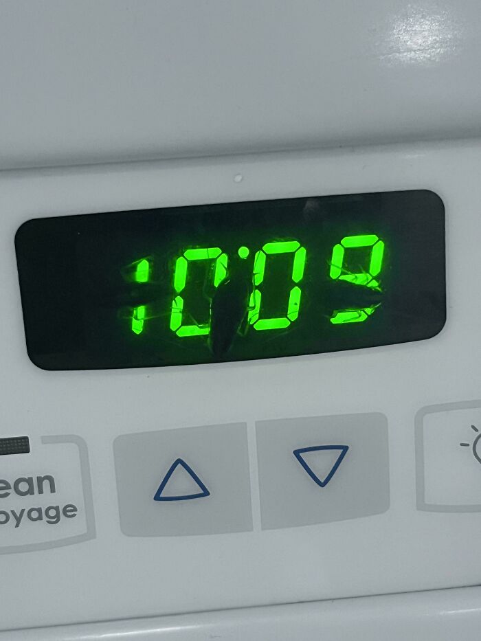 Green digital clock display shows distorted numbers resembling creepy or weird shapes on a white appliance panel.