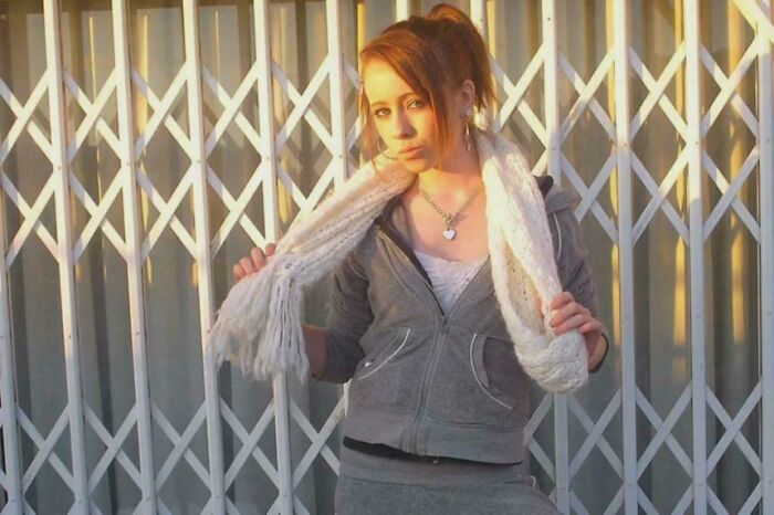 Young woman posing with a white scarf in front of a metal gate, evoking unsettling mysteries that continue to fascinate and disturb.
