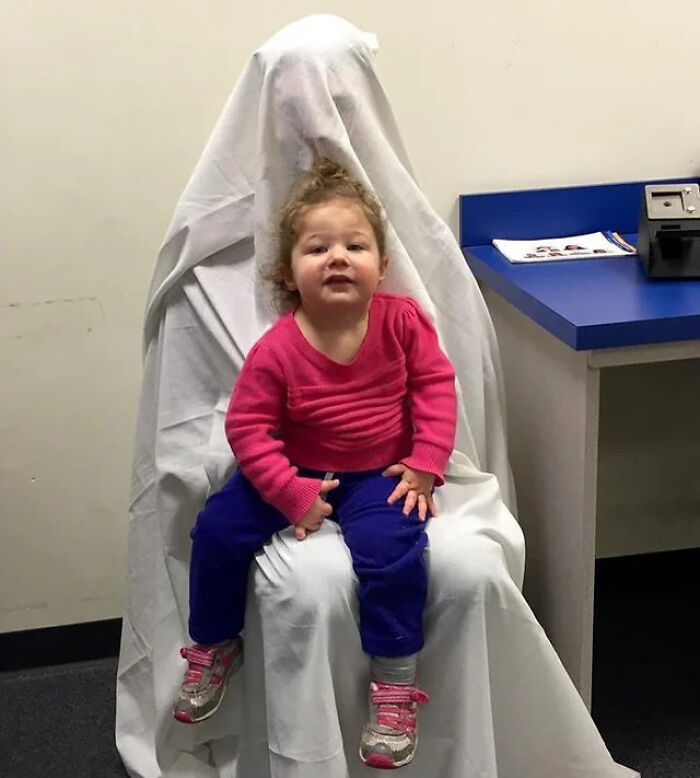 Toddler sitting on a chair covered with a white sheet, creating a creepy and weird photo with heebie-jeebies effect.
