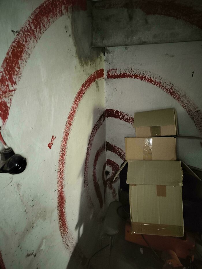 Dimly lit corner with red spiral graffiti on walls and stacked cardboard boxes in a creepy and weird photo setting.
