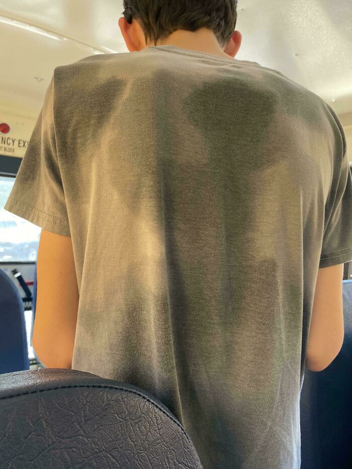 Back of a person wearing a plain t-shirt with sweat patterns creating an unintended, funny design.
