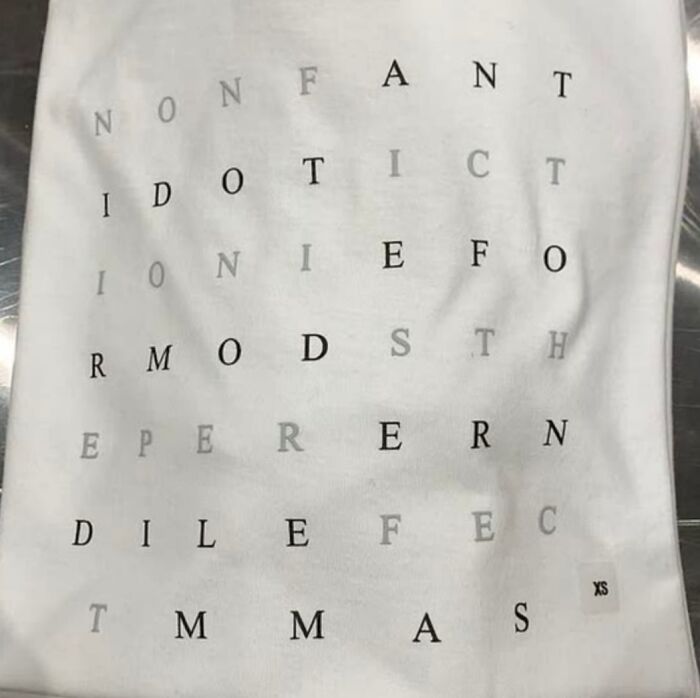 White t-shirt with scattered black and gray letters forming a confusing and humorous design, showcasing bad t-shirt designs.