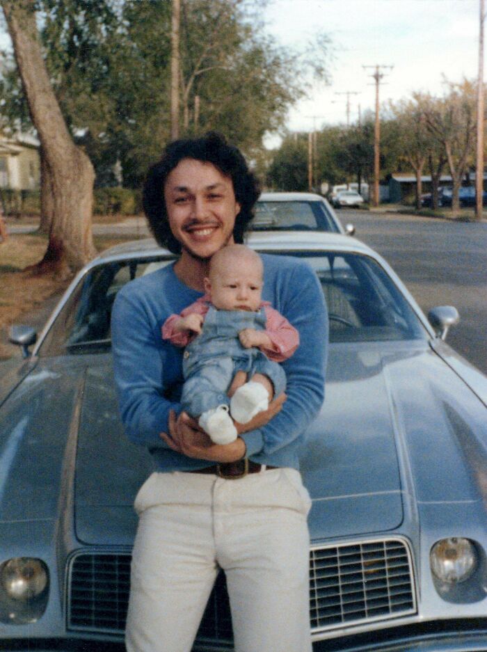 A candid old photo shows a man holding a baby in front of a car, revealing what the world looked like generations ago.