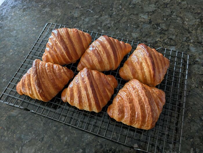 Golden croissants cooling on a wire rack on a dark countertop