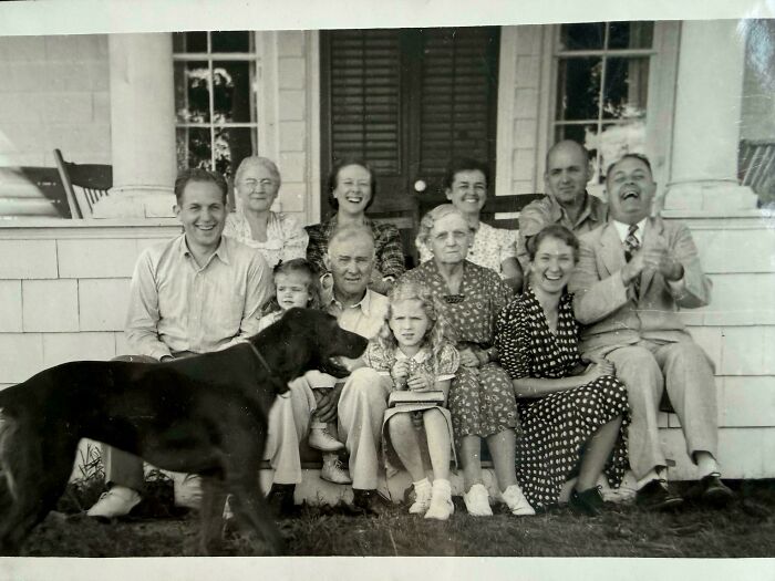 A candid old photo shows a large family and a dog posing on a porch, revealing what the world looked like generations ago.