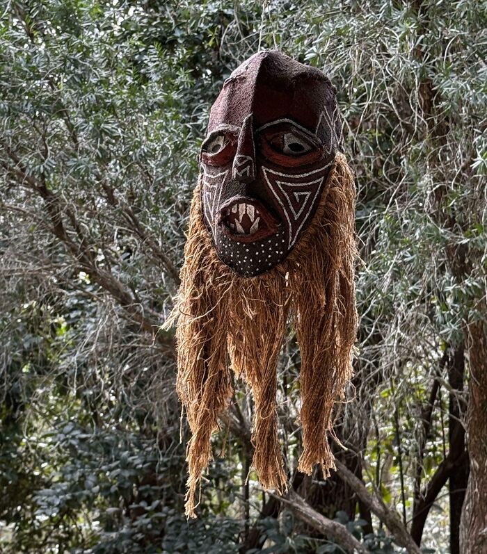 Creepy and weird mask with tribal patterns hanging in a dense forest, evoking eerie and unsettling feelings.