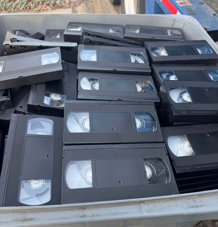 A container filled with old VHS tapes stacked haphazardly, evoking creepy and weird nostalgia vibes.